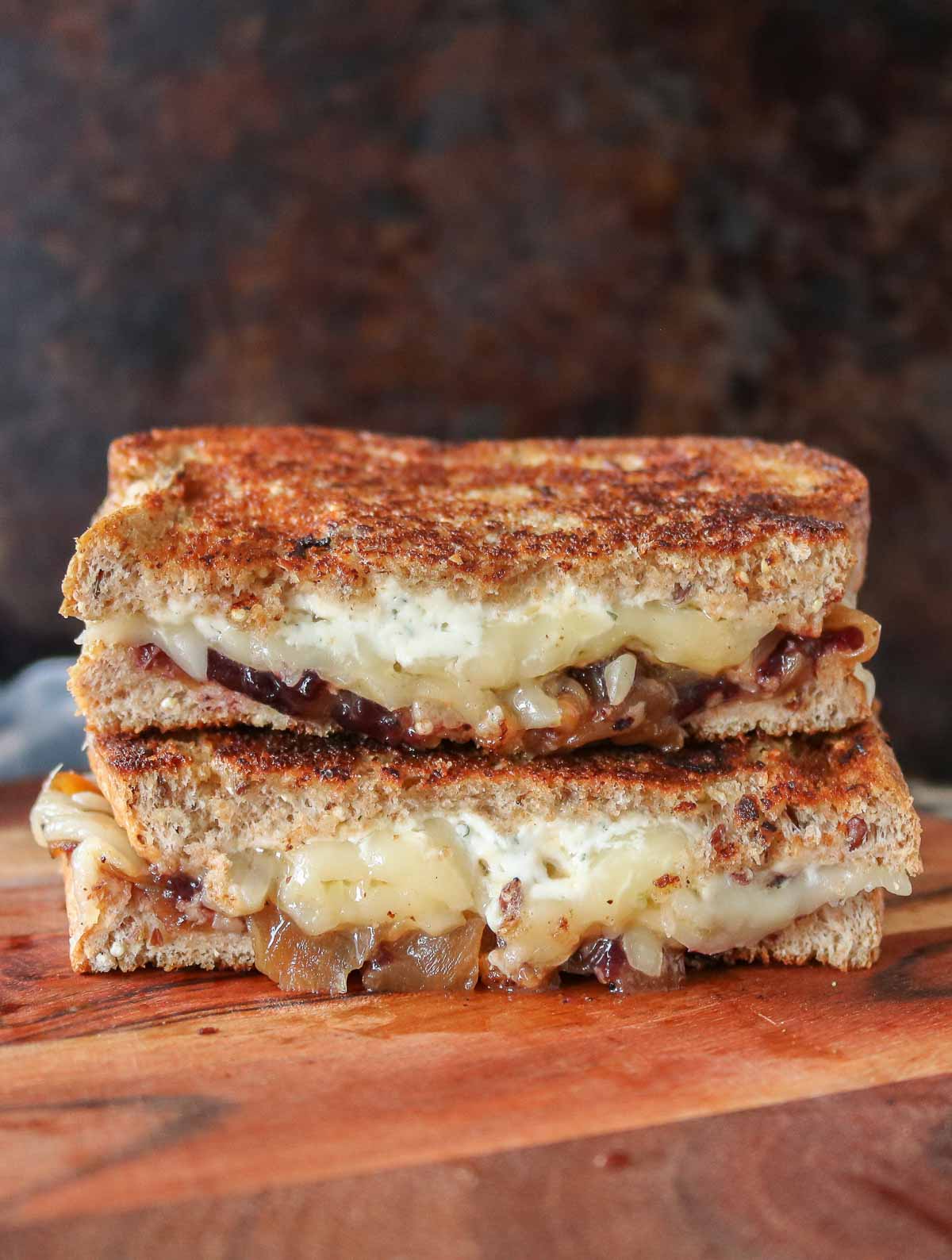 Two halves of a caramelized onion grilled cheese sandwich stacked on a wooden serving board.