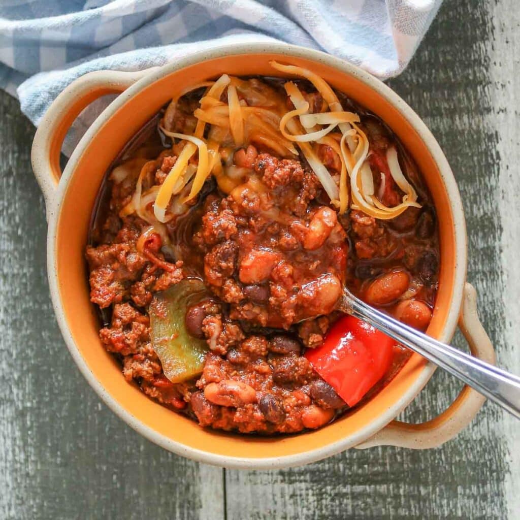 Bowl of chili topped with shredded cheddar cheese.