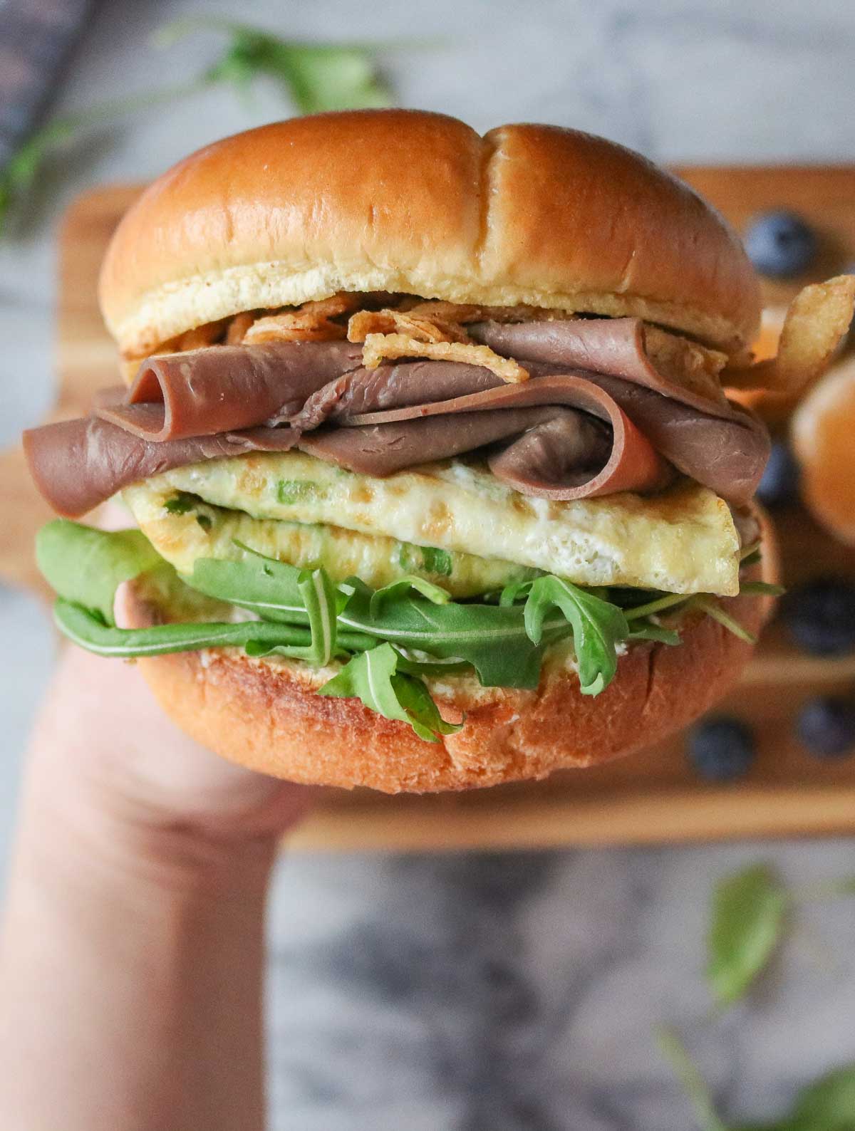 Hand holding a roast beef and egg sandwich.