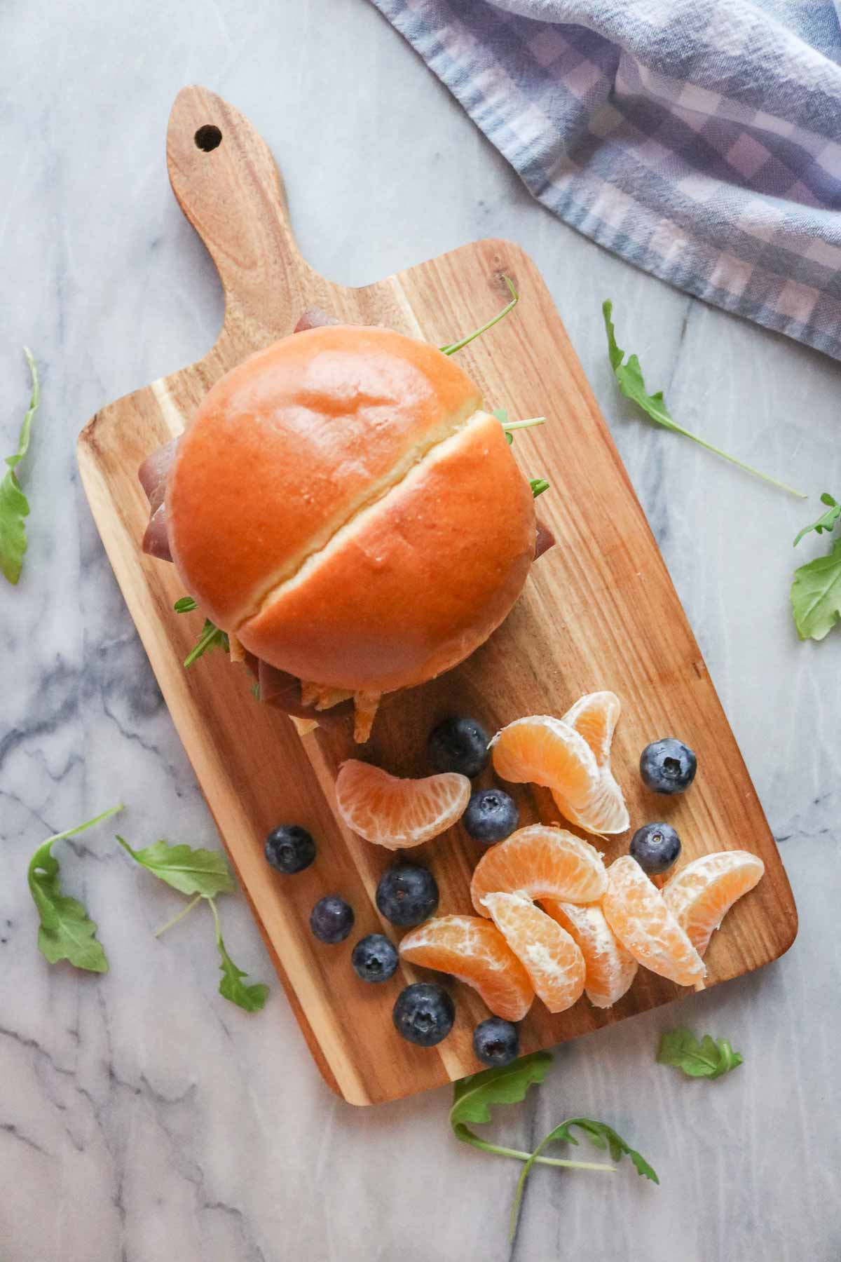 Sandwich alongside clementine wedges and blueberries on a serving board.