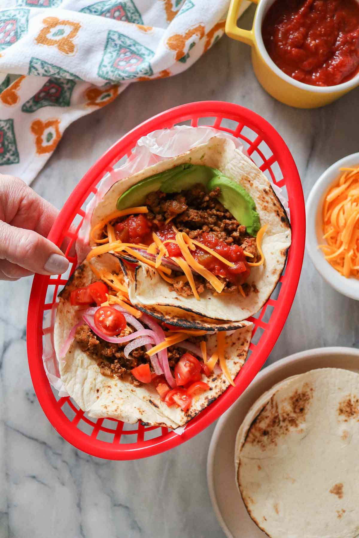 Hand holding a red basket with two ground chicken tacos in it.