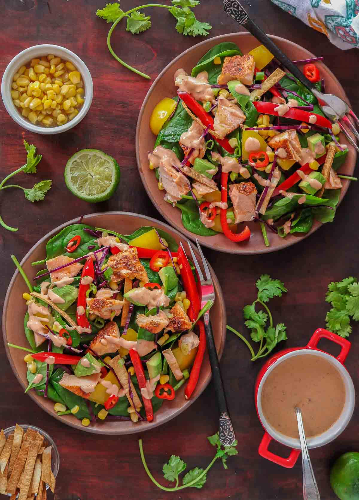 Two bowls of salmon spinach salad drizzled with chipotle dressing.