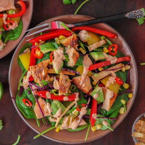 Salmon spinach salad in a bowl drizzled with chipotle dressing.