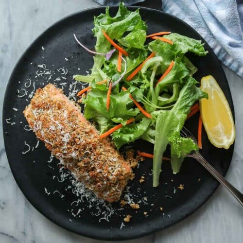 Portion of baked salmon, green salad and lemon wedge on a plate with a fork.