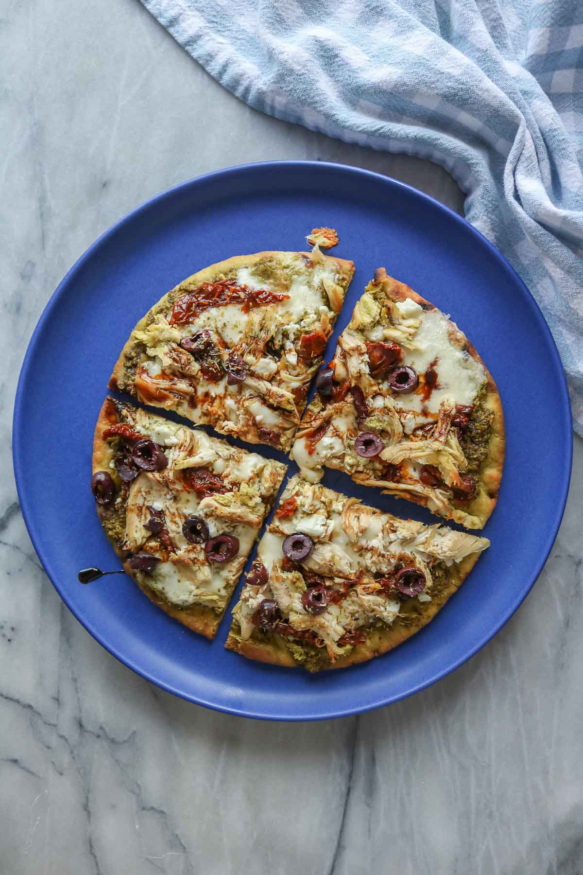 Chicken pesto pizza on a plate cut into four slices.