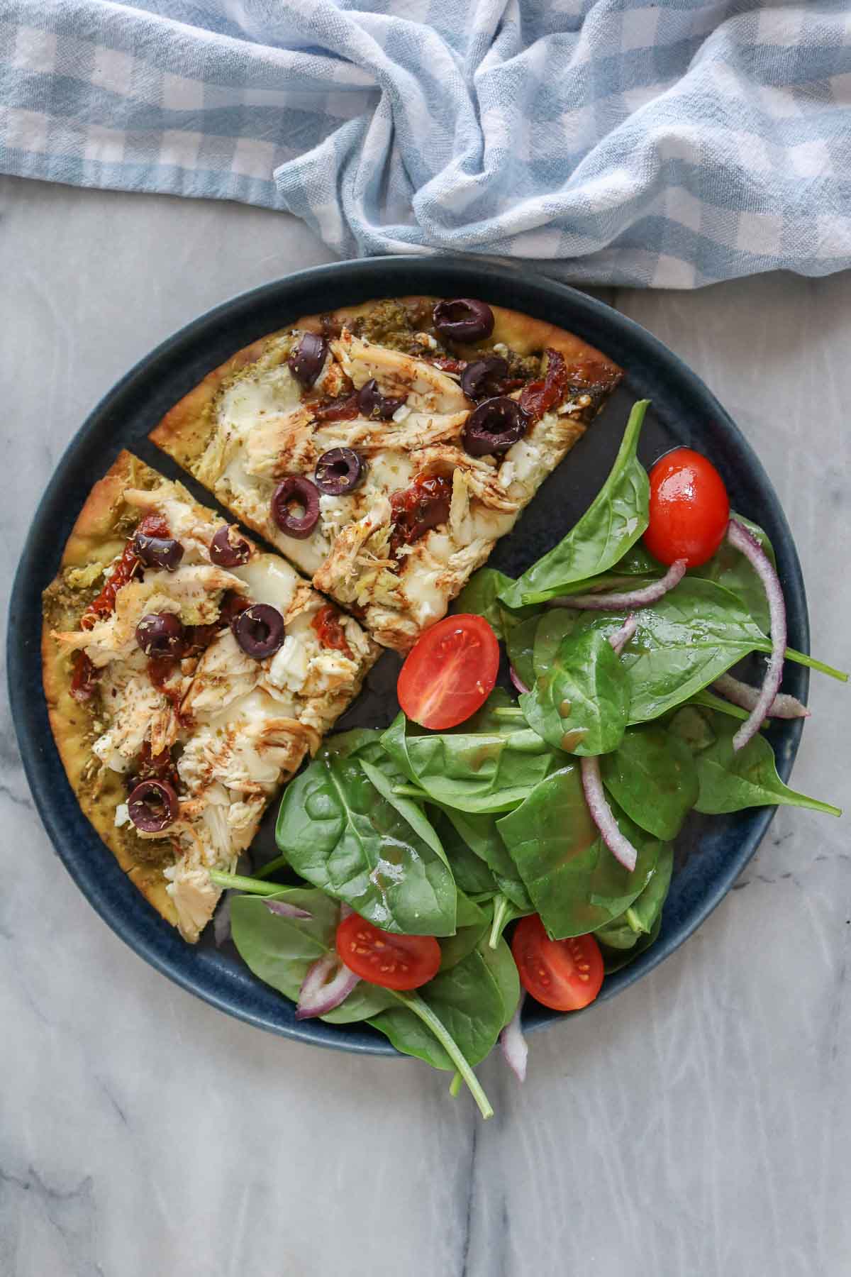 Two slices of chicken pesto pizza on a plate with spinach salad.