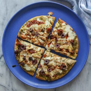 Chicken pesto pizza on a plate cut into four slices.