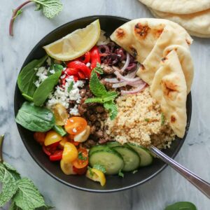 Lamb hummus bowl with naan and a lemon wedge.