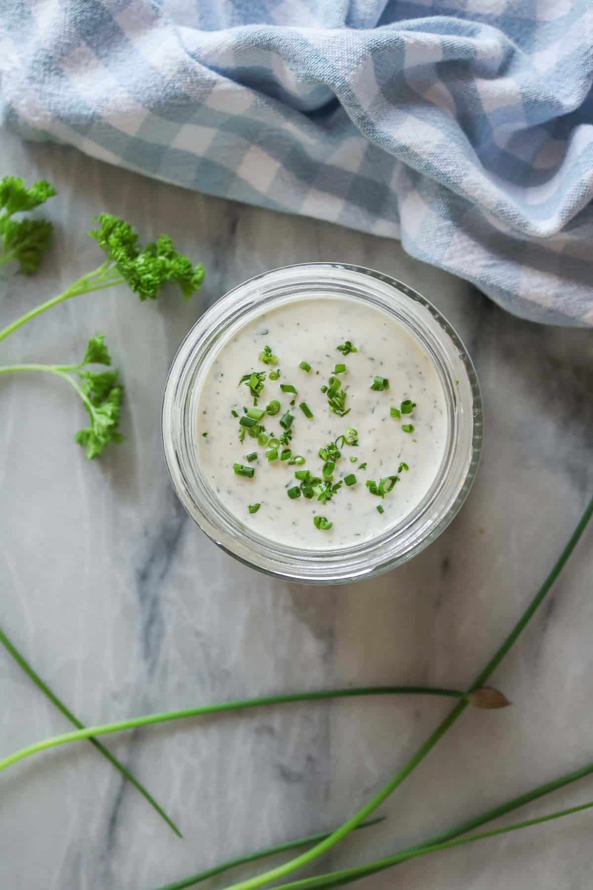 Overhead shot of a jar of homemade ranch dressing with chives and parsley on top.