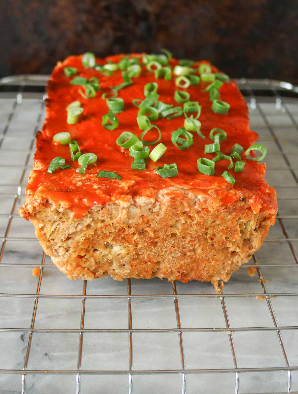 Buffalo chicken meatloaf on a cooling rack garnished with green onion.