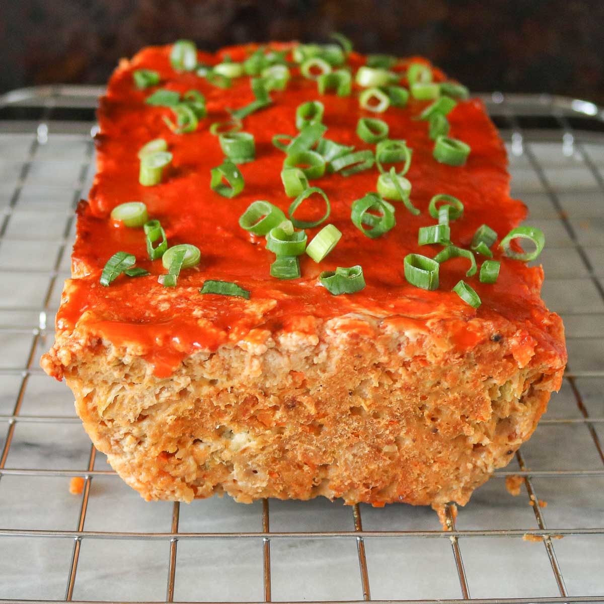 Buffalo chicken meatloaf on a cooling rack garnished with green onion.