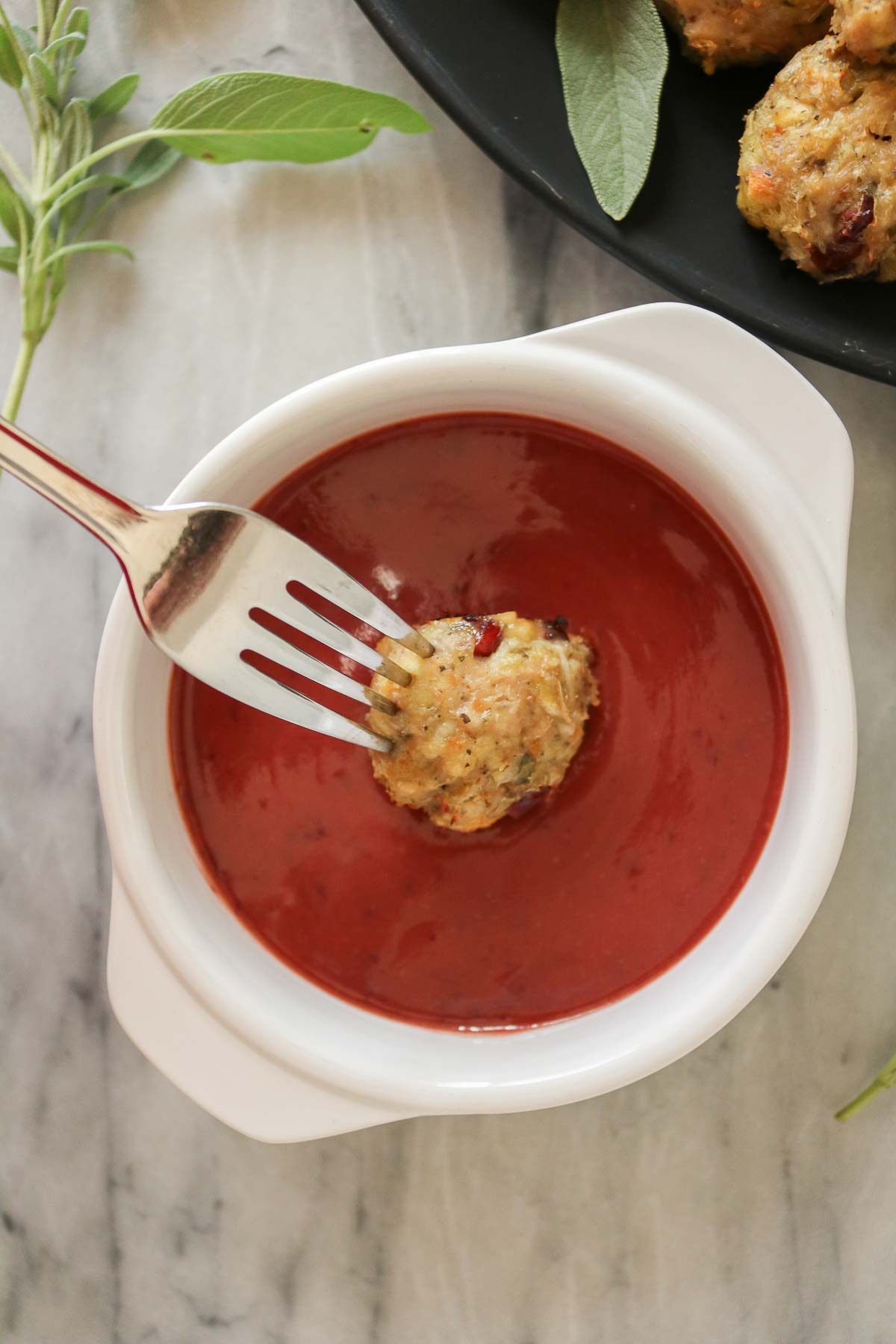 Fork dipping a stuffing chicken meatball into cranberry mustard sauce.