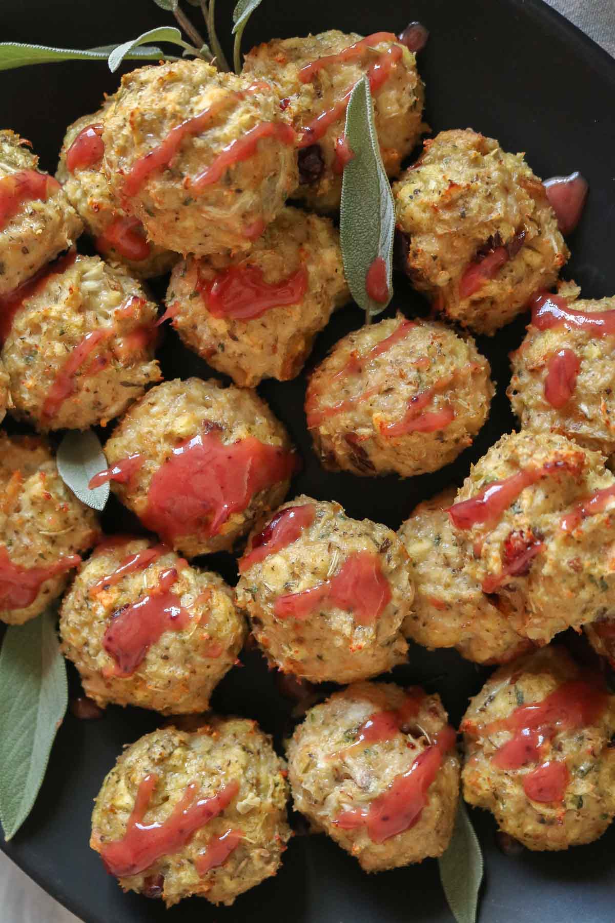 Close-up of stuffing chicken meatballs on a black platter drizzled with cranberry mustard sauce.
