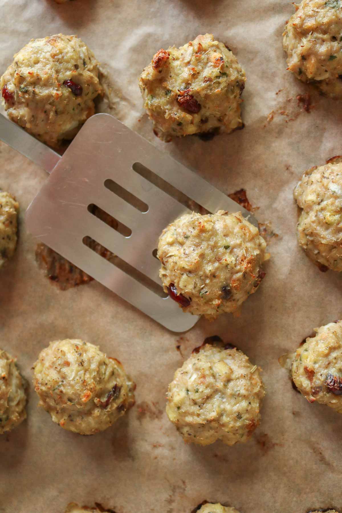 Spatula serving a chicken meatball from a parchment paper-lined sheet pan.