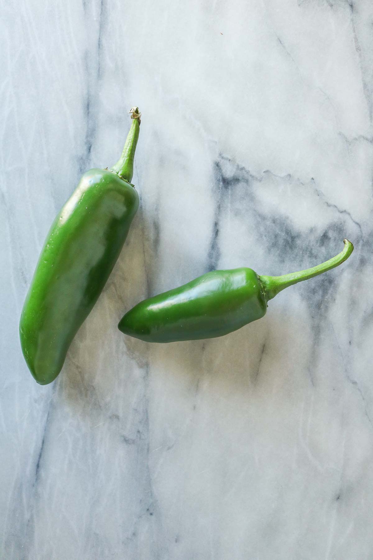Two fresh jalapeno peppers on a marble board.