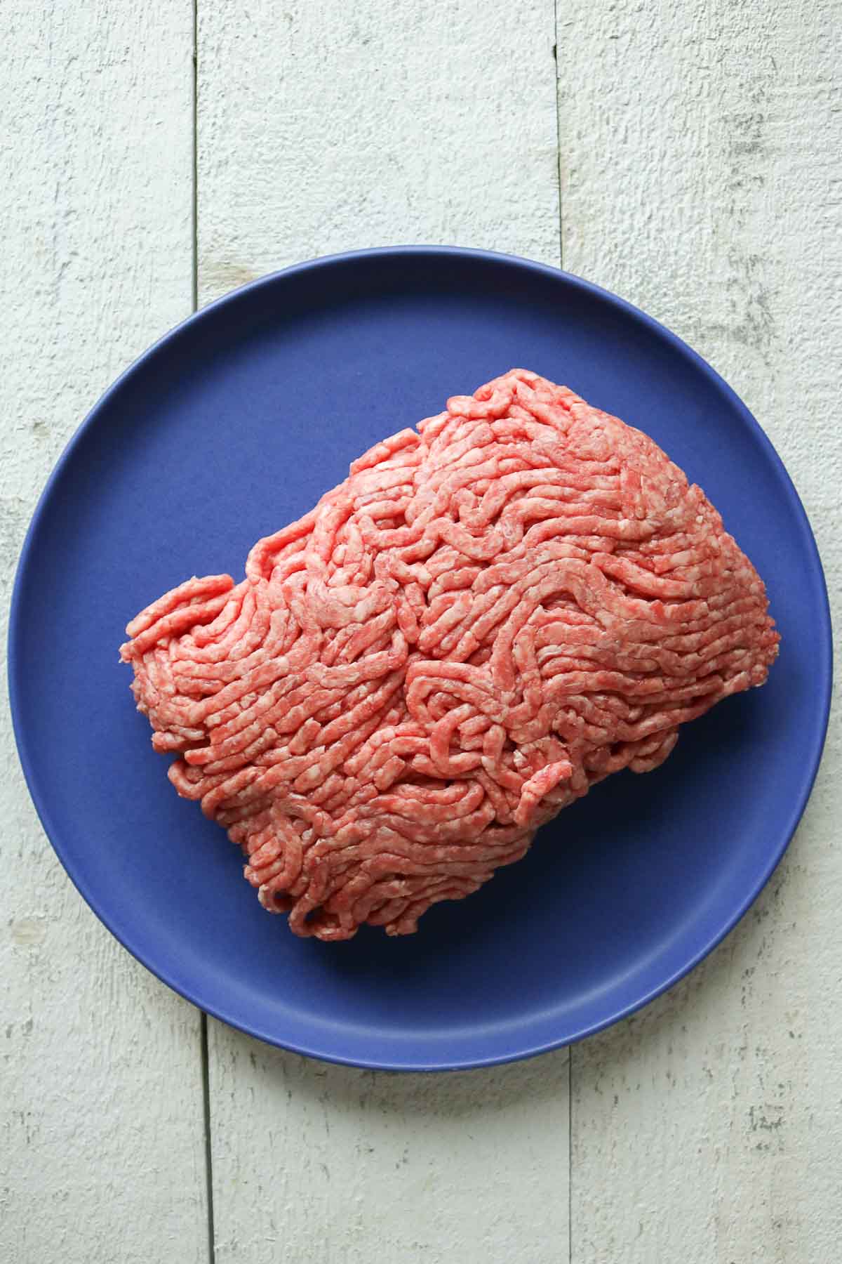 Uncooked lean ground beef on a blue plate.