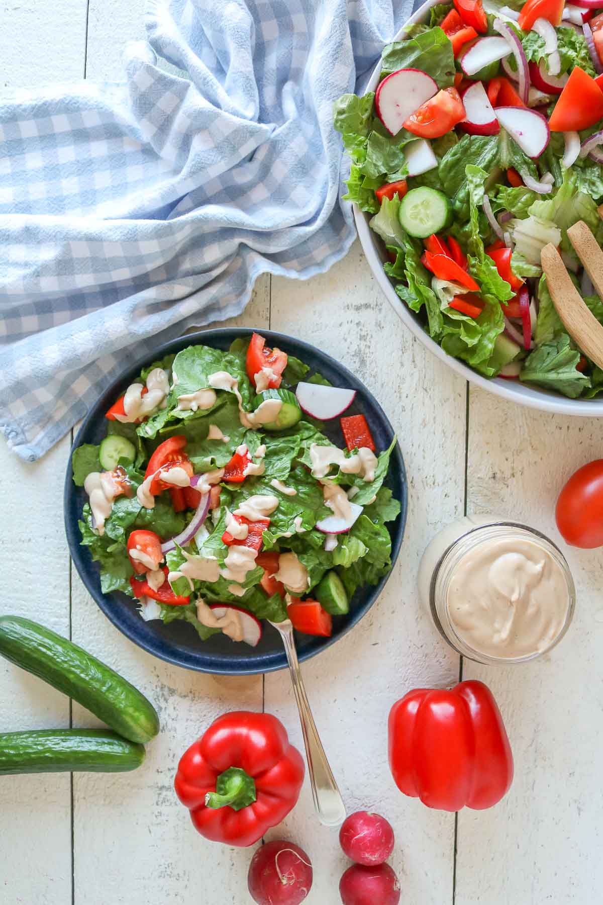 Serving of garden salad on a plate next to a serving bowl of salad.