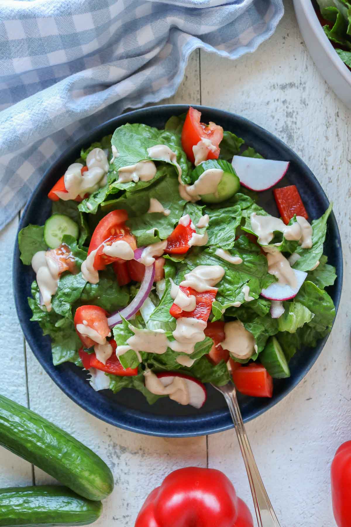 Serving of garden salad on a plate drizzled with creamy dressing.