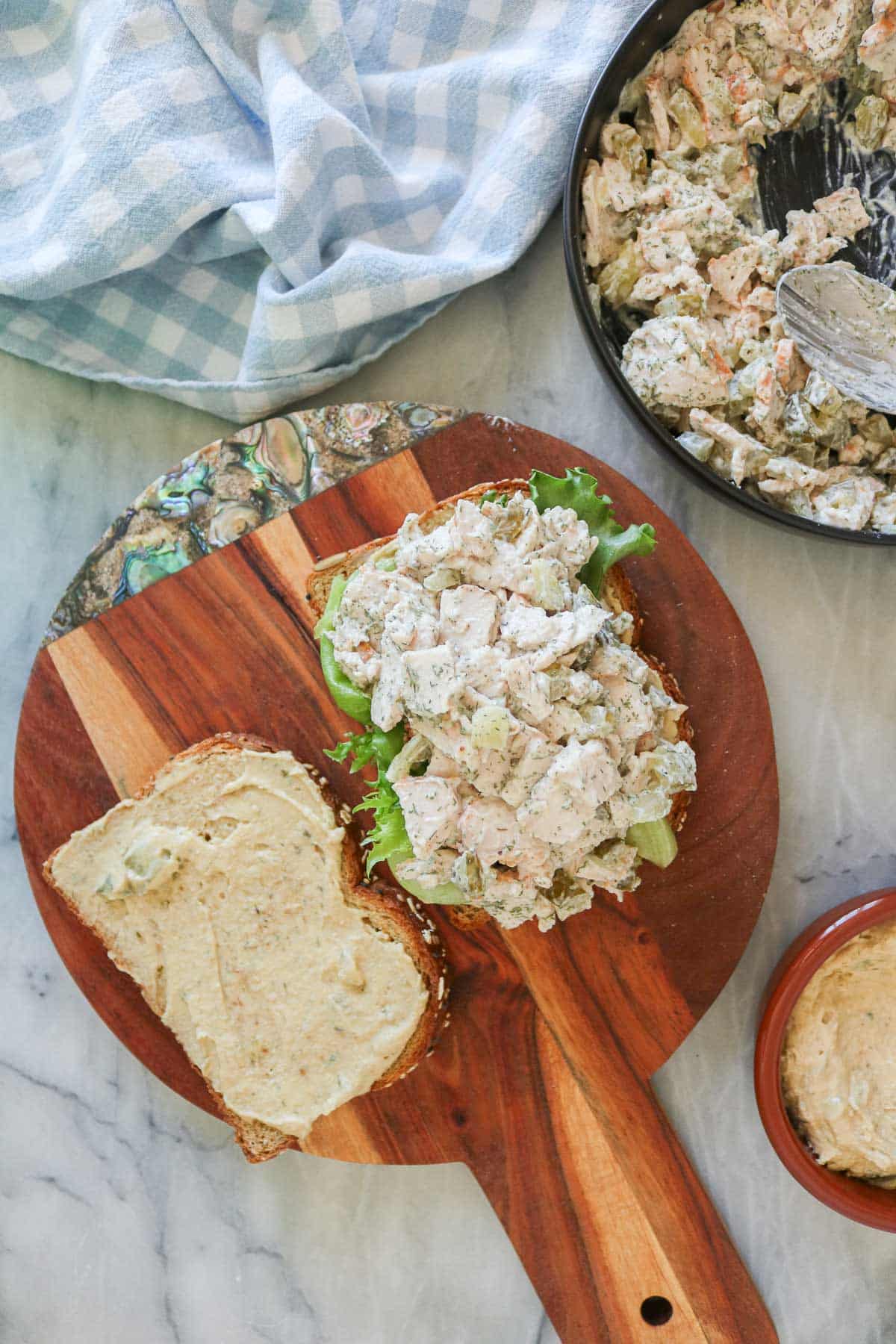 Assembling a dill pickle turkey salad sandwich with lettuce and hummus.