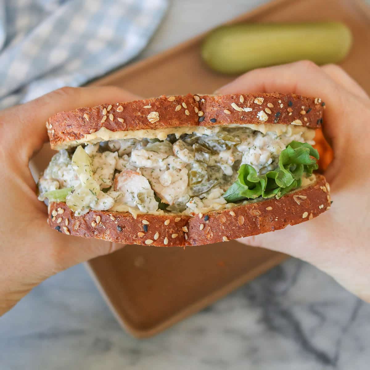 Two hands holding a dill pickle turkey salad sandwich.