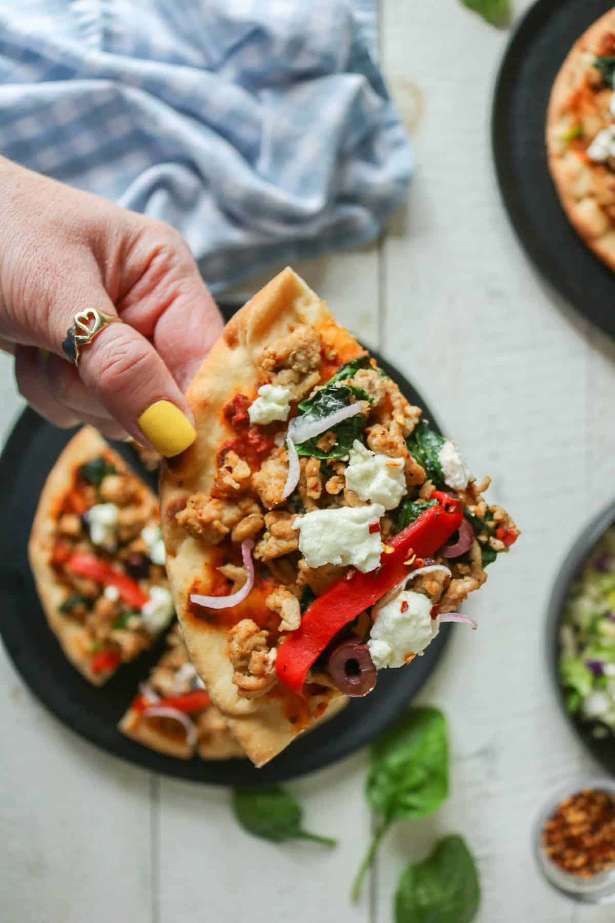 Hand holding a slice of ground chicken pesto pizza.