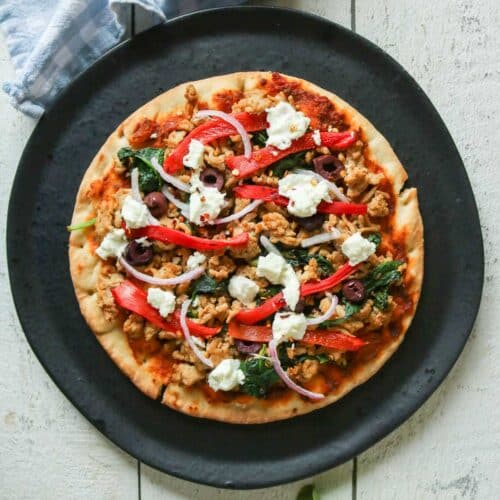 Ground chicken pesto pizza on a black plate before being cut into slices.