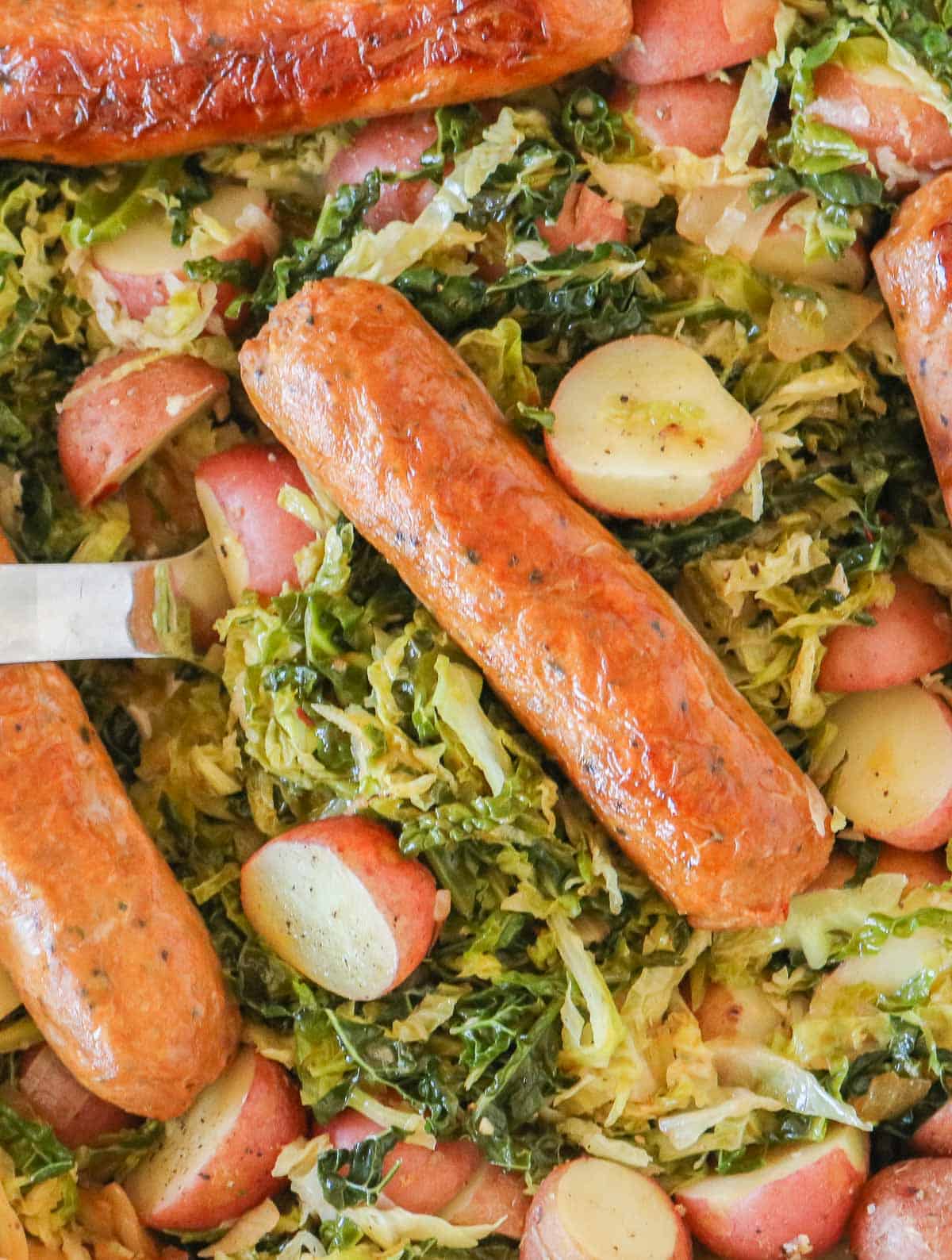 Close up of a serving spoon serving some sausage, cabbage and potatoes from a sauté pan.