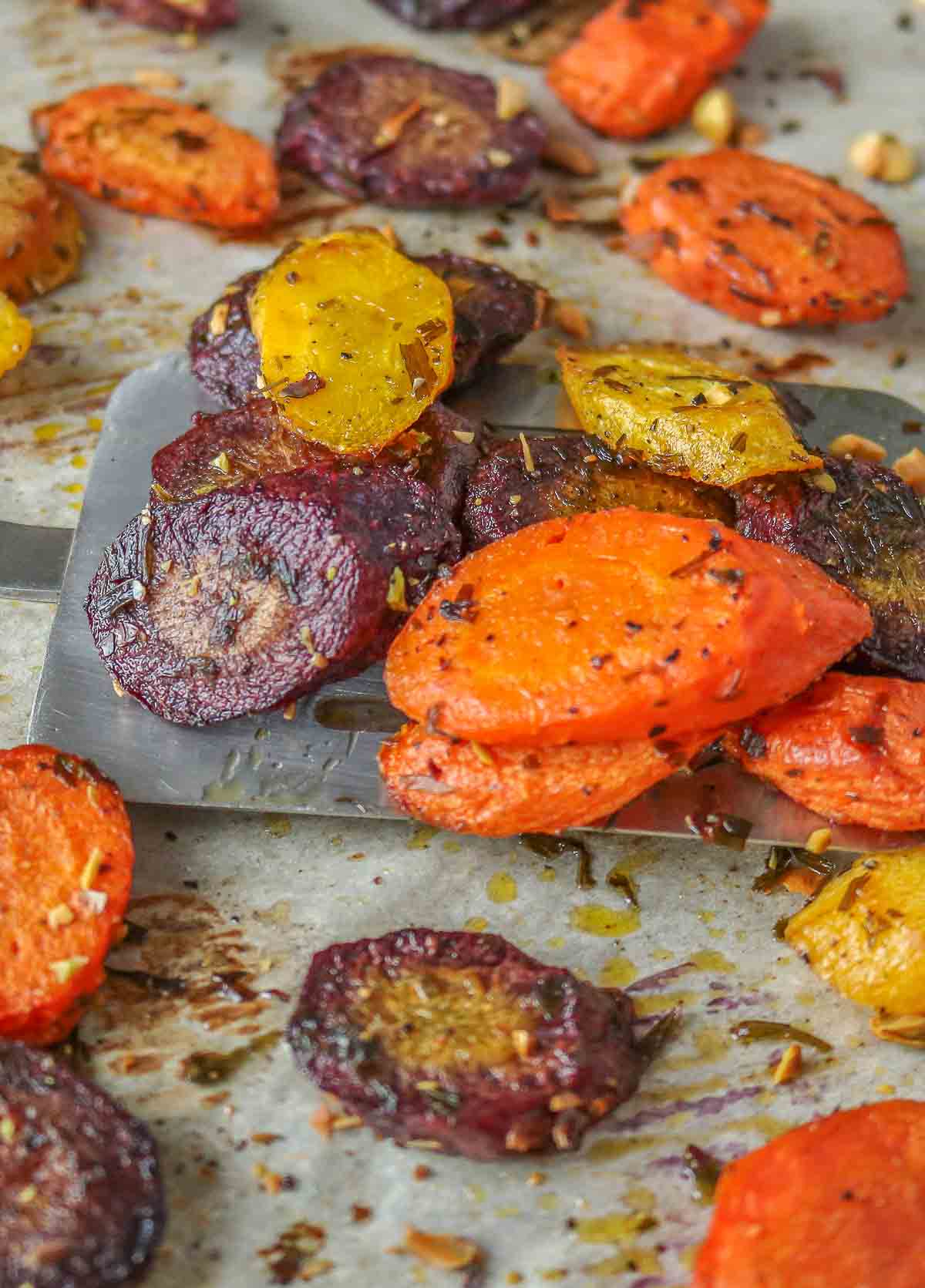 Spatula serving chunks of roasted rainbow carrots from a sheet pan.