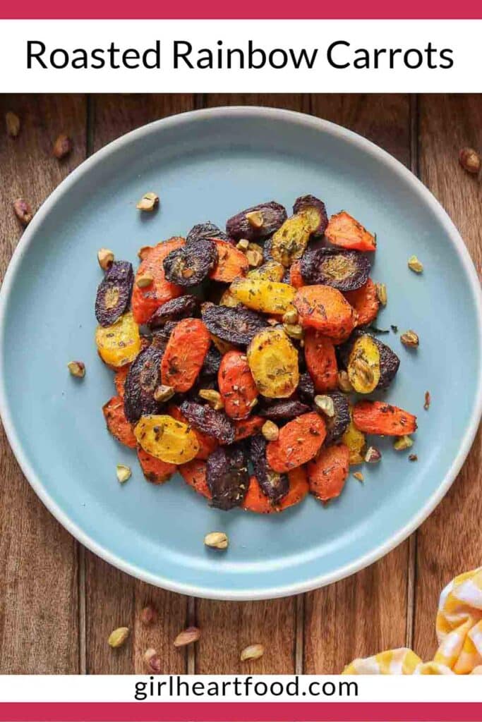 Chunks of roasted rainbow carrots on a blue plate topped with chopped pistachios.