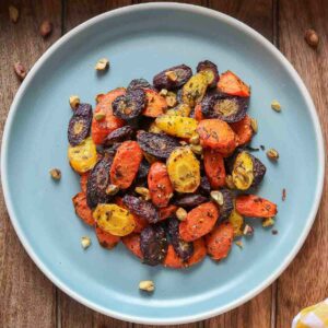 Chunks of roasted rainbow carrots on a blue plate topped with chopped pistachios.