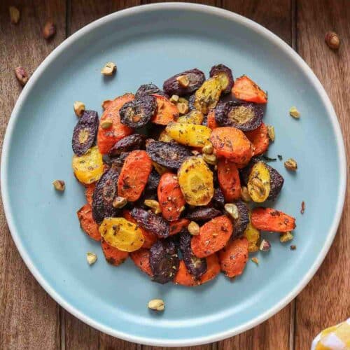 Chunks of roasted rainbow carrots on a blue plate topped with chopped pistachios.